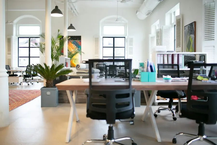 Empty modern office with rows of desks, chairs and potted plants